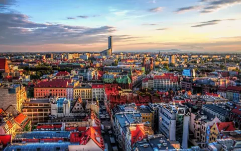 Widok na Wrocław, największe miasto zachodniej Polski, z dominującym wieżowcem Sky Tower. Słońce zachodzi nad kolorowymi dachami kamienic.