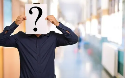 Un homme en chemise bleue cache son visage derrière un point d'interrogation. Une métaphore visuelle pour la quête : comment retrouver une personne sans son nom et prénom ?