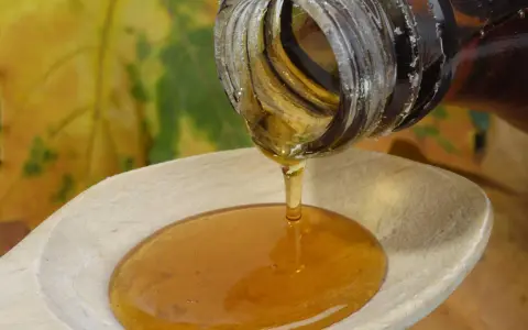 Ahornsirup tropft aus einer Flasche auf einen Holzlöffel. Die Frage, ob kann ahornsirup schlecht werden, beschäftigt viele.