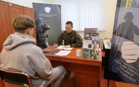 Młody mężczyzna rozmawia z żołnierzem w punkcie rekrutacyjnym. Dyskutują o możliwościach związanych z obowiązkową służbą wojskową.