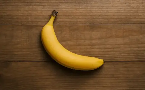 Eine gelbe Banane liegt auf einem Holztisch. Sie ist ein gesunder Snack, aber wie viel Protein hat eine Banane?