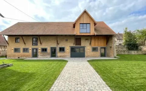 Belle grange rénovée avec une façade en briques jaunes, un toit en tuiles et un ajout moderne en bois. Un chemin pavé mène à l'entrée principale.