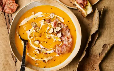 Velouté de courge onctueux, garni de noisettes croquantes, d'une touche de crème et d'une tranche de bacon croustillant. Un délice automnal qui évoque le beurre de courge.