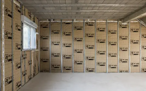 Le chantier progresse, on commence à isoler un mur avec des panneaux Isover. Une fenêtre est visible sur la gauche.