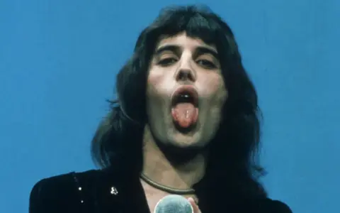 Freddie Mercury z wyciągniętym językiem, śpiewający do mikrofonu. W jego oczach widać pragnienie, by **break free**.
