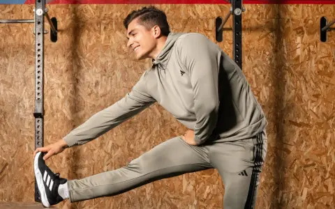 Ein Mann in Trainingskleidung macht dynamisches Dehnen vor einer Holzwand.