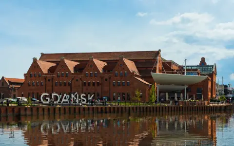 Gdańsk zwiedzanie: ceglane kamieniczki nad Motławą, wielki napis "GDAŃSK" i odbicie w wodzie.