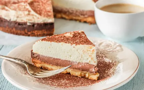 Pyszna tarta z mascarpone i czekoladą, posypana kakao, czeka na widelczyk. Obok filiżanka kawy.