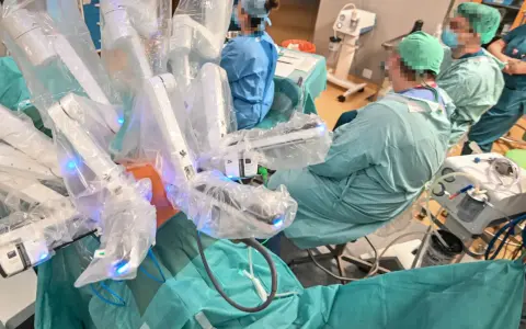 Chirurdzy w zielonych fartuchach prowadzą operację prostaty da Vinci. Robotyczne ramiona systemu są widoczne, pokryte sterylnymi osłonami.