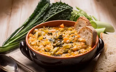 Una ciotola di ribollita fumante, ricca di verdure e fagioli, accompagnata da fette di pane tostato e cavolo nero.
