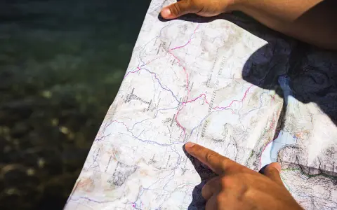 Une main pointe un itinéraire sur une carte topo détaillée, près d'une étendue d'eau.
