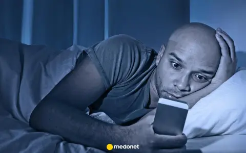 Mężczyzna leży w łóżku, wpatrując się w telefon. Czy to już obsesja?