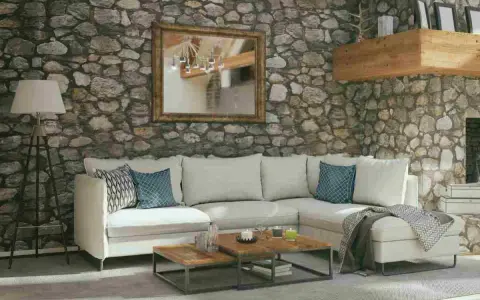 Soggiorno accogliente con pareti in pietra grezza, divano bianco, tavolini in legno e specchio dorato. Ottime idee pareti in pietra per un ambiente rustico.