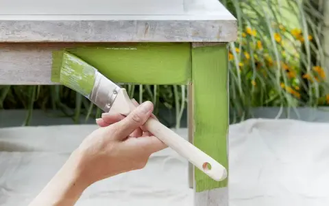 Mano pintando una mesa de madera con pintura verde brillante. El proceso de pintar con tizas da un acabado rústico y encantador.