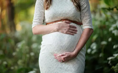 Kobieta w białej sukience obejmuje ciążowy brzuch. To piękny moment, kiedy można zajść w ciążę i poczuć nowe życie.