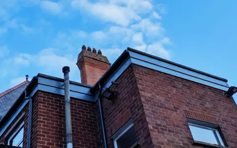 Vue d'une maison en briques rouges avec une cheminée traditionnelle et un conduit de poêle à bois sortie ventouse en façade. Ciel bleu avec quelques nuages.