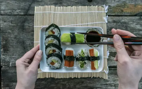 En bricka med olika sorters sushi, perfekt för ett enkelt sushi recept. En hand håller ätpinnar redo att plocka upp en bit.