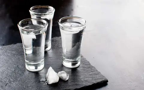 Drei Gläser Wodka mit Eiswürfeln auf dunklem Stein. Wodka wird aus Getreide oder Kartoffeln hergestellt.