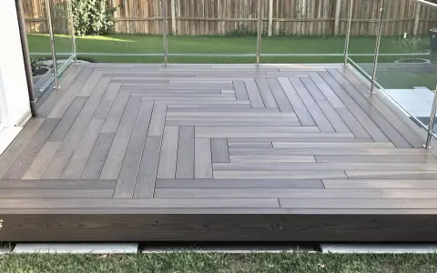 Une belle terrasse bois sur plot béton, avec un motif en chevrons élégant et une balustrade en verre moderne.
