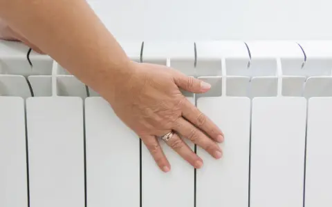 Main posée sur un radiateur électrique blanc, vérifiant la température hors gel.
