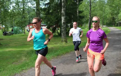 Tre kvinnor springer på en grusväg i en skogsmiljö, zon 2.