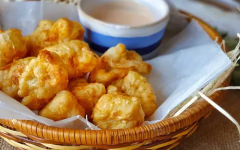 Cesta de mimbre con crujientes fritos de pixin, acompañados de una cremosa salsa rosa. ¡Un bocado delicioso!
