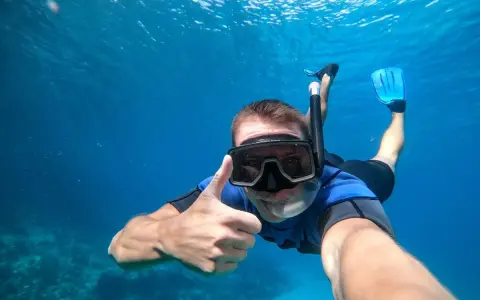 En man snorklar och ger tummen upp i det klara vattnet vid Nerja strand.