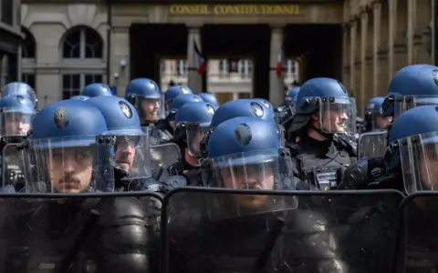 Un grupo de gendarmes con cascos azules y escudos protectores se prepara para mantener el orden frente al Conseil Constitutionnel.
