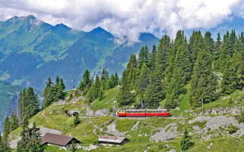 A red and yellow cogwheel train winds through the Swiss Alps, a scenic way to get around Interlaken.