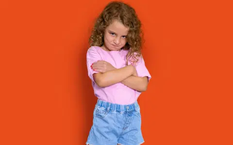 Niña con rizos, brazos cruzados y expresión de enfado. Podría representar la **depresión infantil** o simplemente un mal humor pasajero.