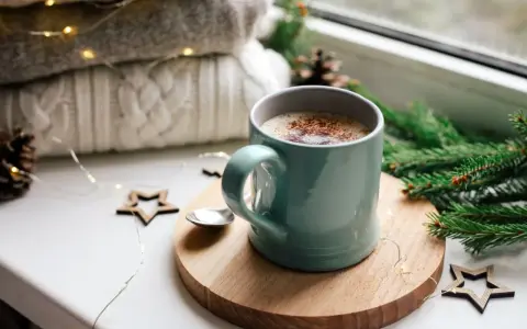 Une tasse de chocolat chaud fumant, entourée de décorations de Noël et de lumières scintillantes, promet un moment de réconfort.
