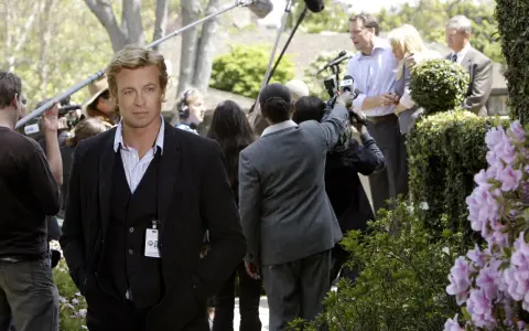 Simon Baker, con la sua nuova fidanzata, è circondato da telecamere e microfoni durante un evento all'aperto.