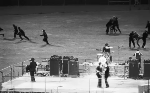 En kaotisk scen med figurer som springer, kanske en representation av The Beatles sista spelning.