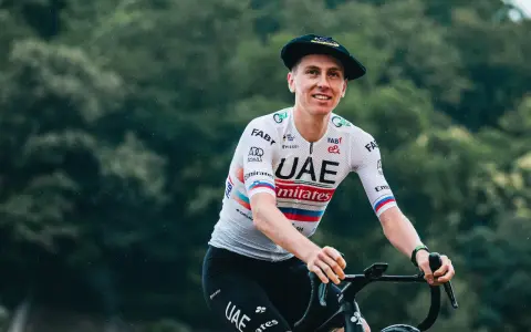 Tadej Pogačar, known for his incredible VO2 max, smiles while riding his bike in a UAE Emirates jersey and a Basque beret.