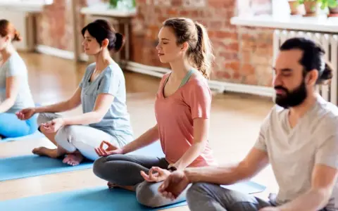 Menschen in einem Yogastudio praktizieren Stress-Meditation, sitzen im Lotussitz auf Matten und schließen die Augen.