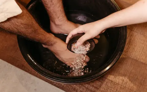 A hand pours pink salt into a foot bath, a natural substitute for Epsom salt to soak tired feet.
