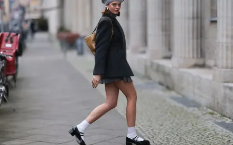 Dziewczyna w stylu Marry Jane, w szarej beretce i krótkiej spódniczce, idzie ulicą.
