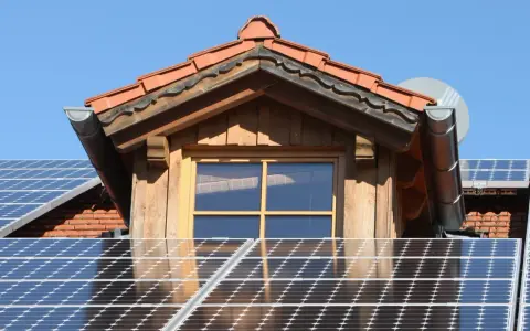 Dach mit Solarmodulen, die erneuerbare Energie von der Sonne einfangen. Ein Fenster und ein Dachüberstand aus Holz sind sichtbar.