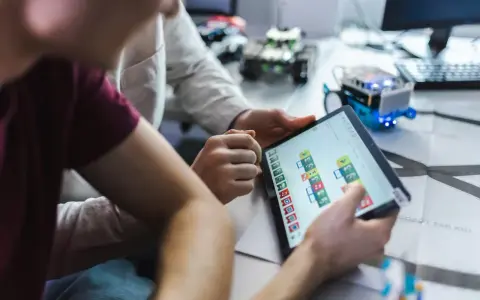 Dzieci programują robota na tablecie, ucząc się, czym zajmuje się informatyk.