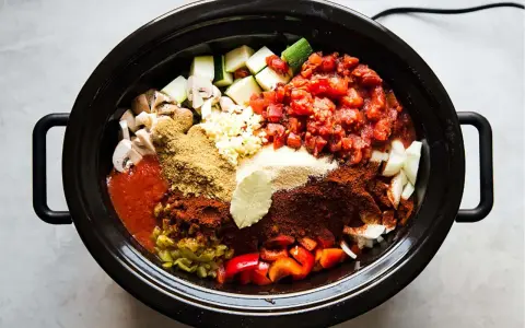 En slow cooker fylld med hackade grönsaker, tomater och kryddor, redo att bli en smakrik gryta.