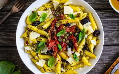 Penne con pesto, pomodori secchi, olive nere, capperi e scaglie di parmigiano. Un piatto colorato e saporito.