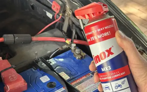 A hand holds a can of INOX MX3 lubricant near a car battery. Does cleaning battery terminals help? This spray might be the answer.