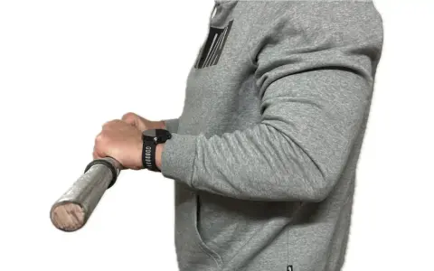 Person in grauem Hoodie macht einen Wrist Curl mit einer Hantel.