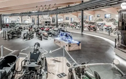 Wnętrze muzeum motocykli pełne zabytkowych maszyn, w tym motocykli z wózkami bocznymi i klasycznych samochodów.