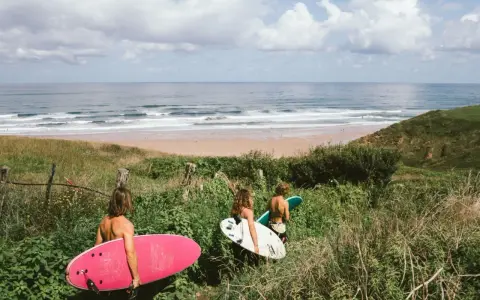 Drei Freunde mit Surfbrettern auf dem Weg zum Strand in Spanien. Die Wellen laden zum Surfen ein.