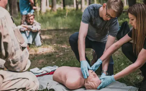 Uczestnicy kursu przetrwania ćwiczą resuscytację na fantomie w lesie.