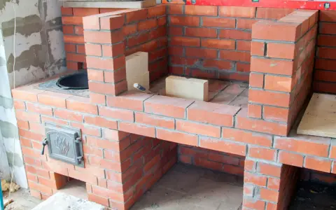 Budowa solidnego grill z cegły klinkierowej. Widać palenisko i drzwiczki.