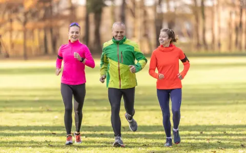 Un gruppo di amici sorridenti segue un programma allenamento corsa e camminata in un parco autunnale.