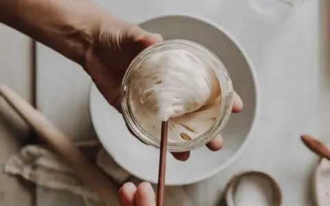 Eine Hand hält ein Glas mit lebendigem Sauerteig, bereit zum Auffrischen. Blasen und Luftlöcher zeigen seine Aktivität.