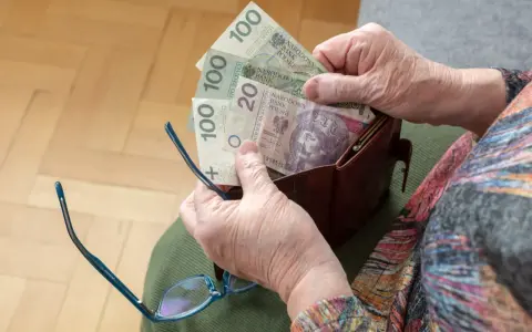 Dłonie starszej osoby wyciągają pieniądze z portfela. Widać banknoty 100 zł i 20 zł, być może to oczekiwana trzynasta emerytura.
